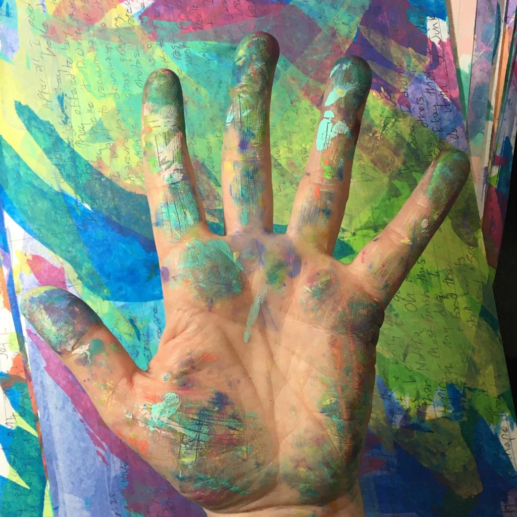 Paint spattered hand, palm up on colorful background