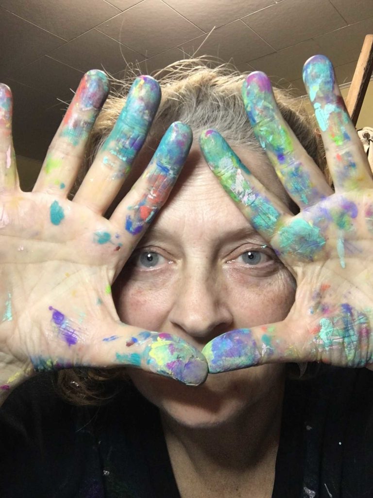 Woman's eyes framed by paint splattered hands, palms out